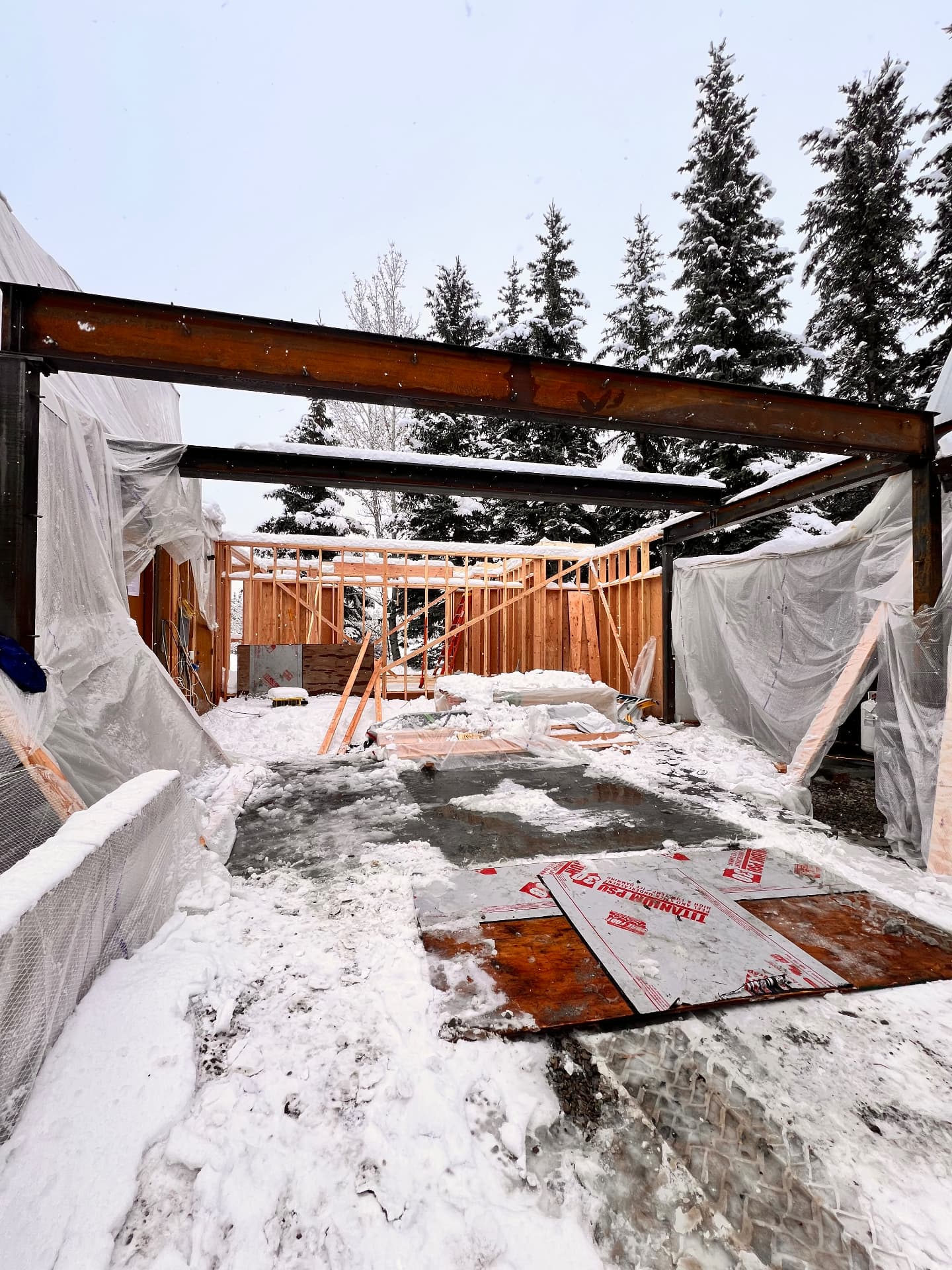 Welded structural steel I-beam frame erected over a snowy residential addition under construction in Idaho