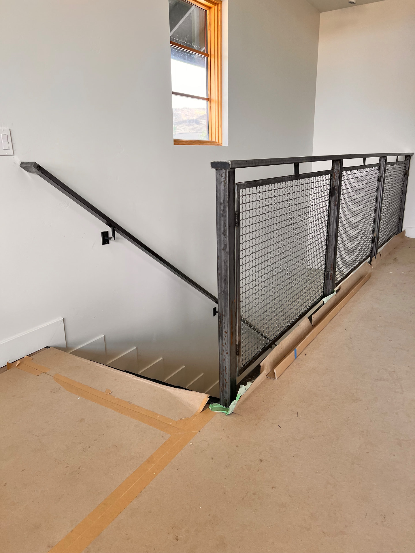Custom steel mesh panel guardrail with matching handrail at an interior stairwell landing under construction
