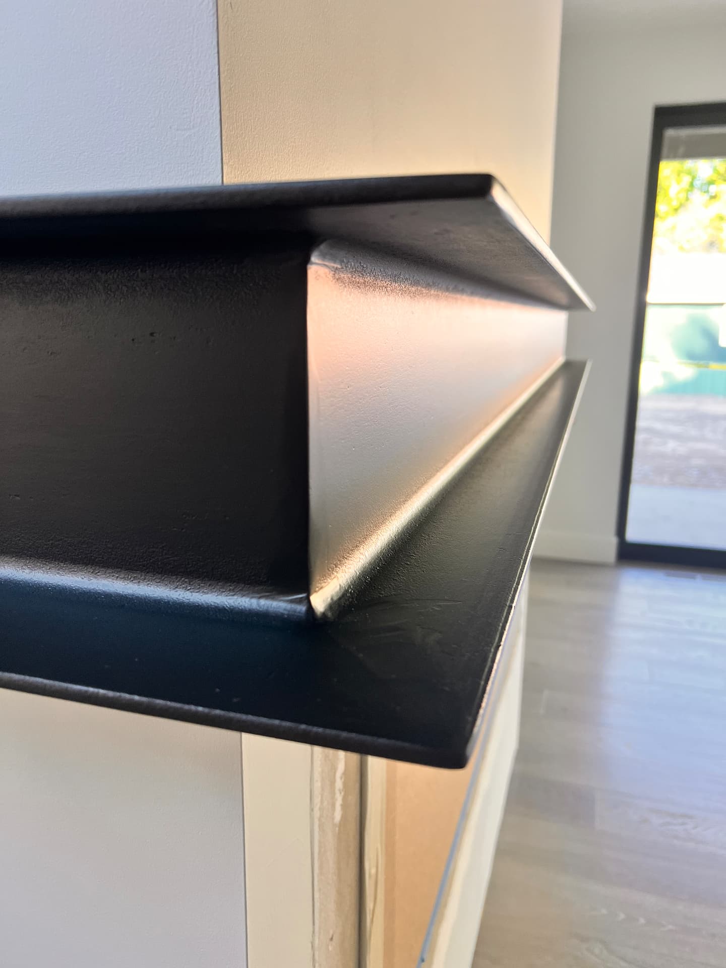 Close-up detail of a precisely welded corner on a custom black steel fireplace mantle