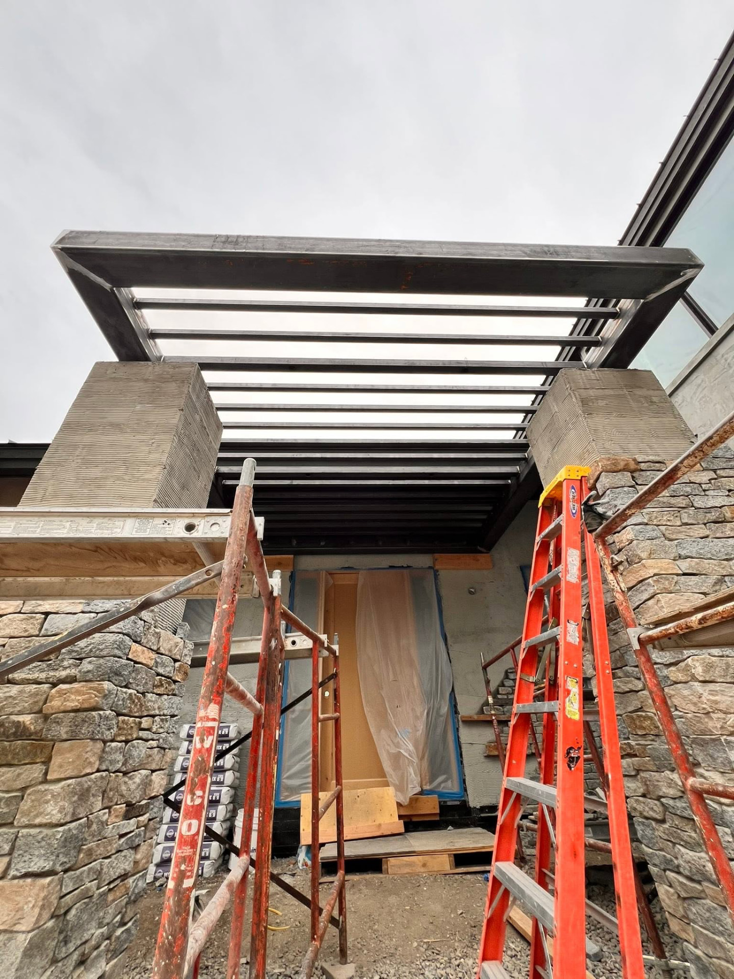 Black steel entry canopy with open rafters framed over a home's front door between stone columns