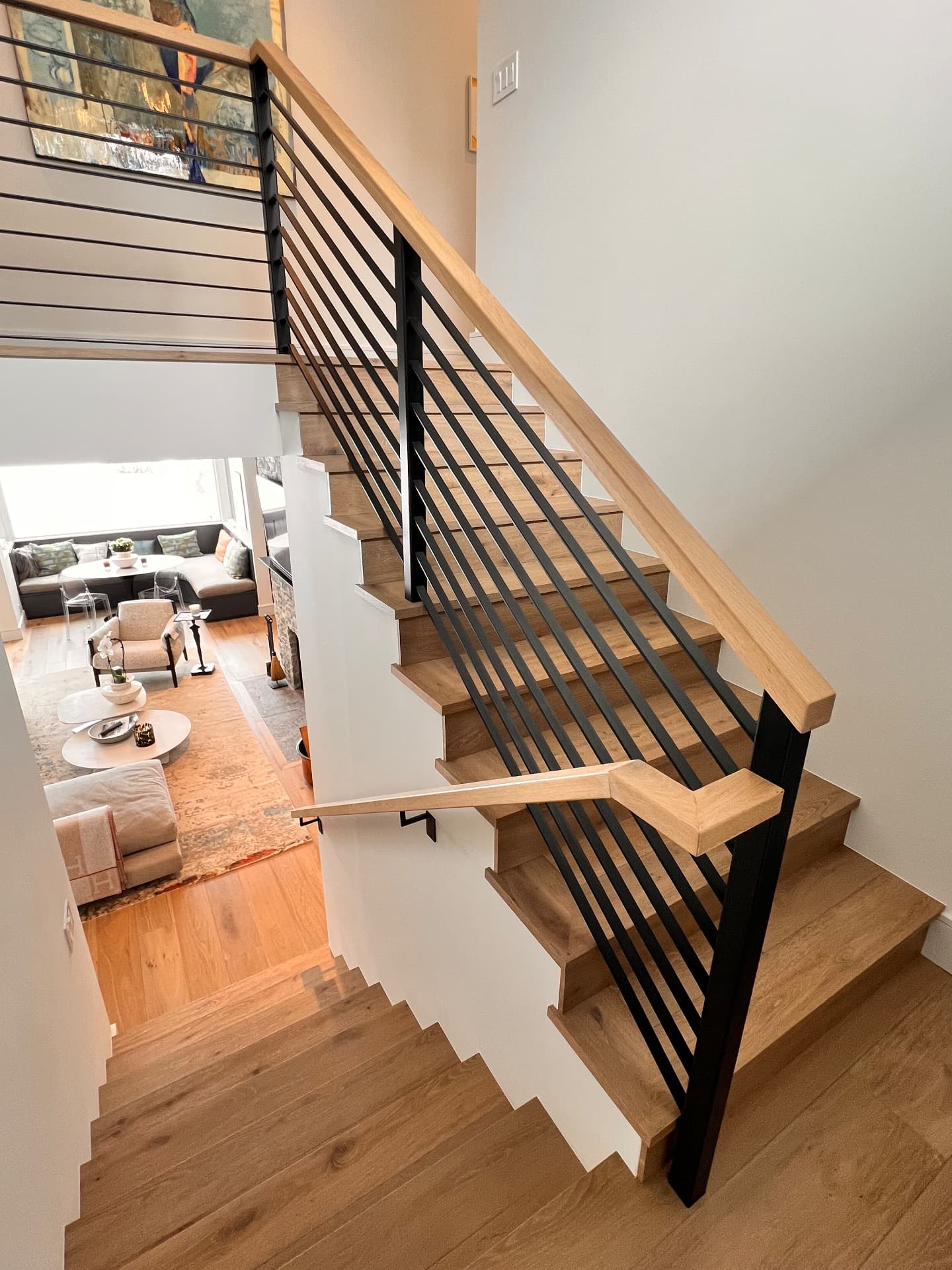 Finished open stairwell with wood treads, wood handrails, and black horizontal steel balusters