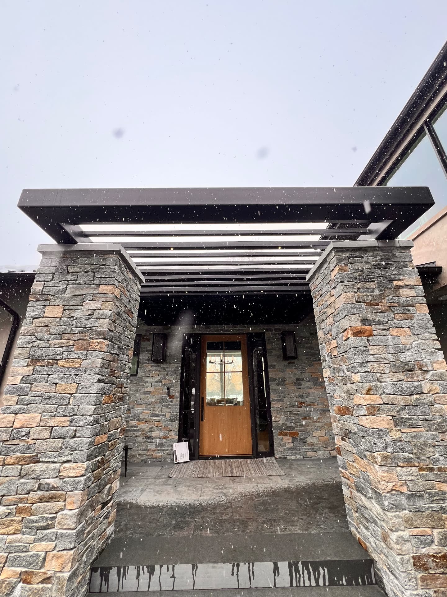 Black steel entry canopy spanning stone columns above a residential front door in winter